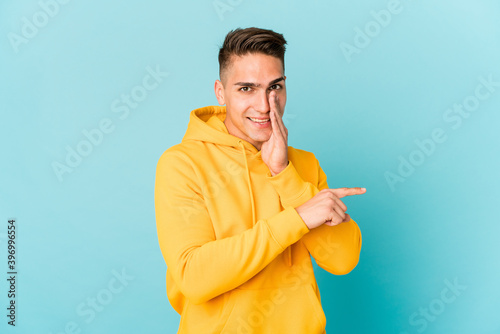 Young caucasian handsome man isolated saying a gossip, pointing to side reporting something.