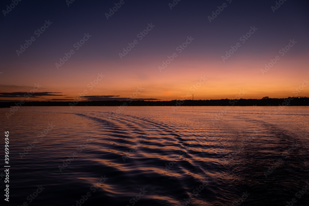 Obraz premium sunset over water from a boat. boat trails. Orange sky