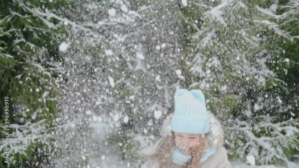 A girl throws snow over herself while standing in the park A girl throws snow over herself while standing in the park
