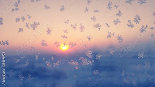 Snowflakes on window in pink morning sunrise cold winter. Blue ice frost, white color snowflakes pattern background. Frosty weather in december, snowflakes on window glass beautiful abstract sunlight