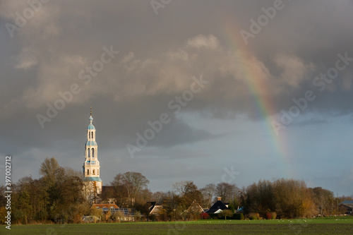 Small rural village with white church tower under dark clouds with rainbow photo