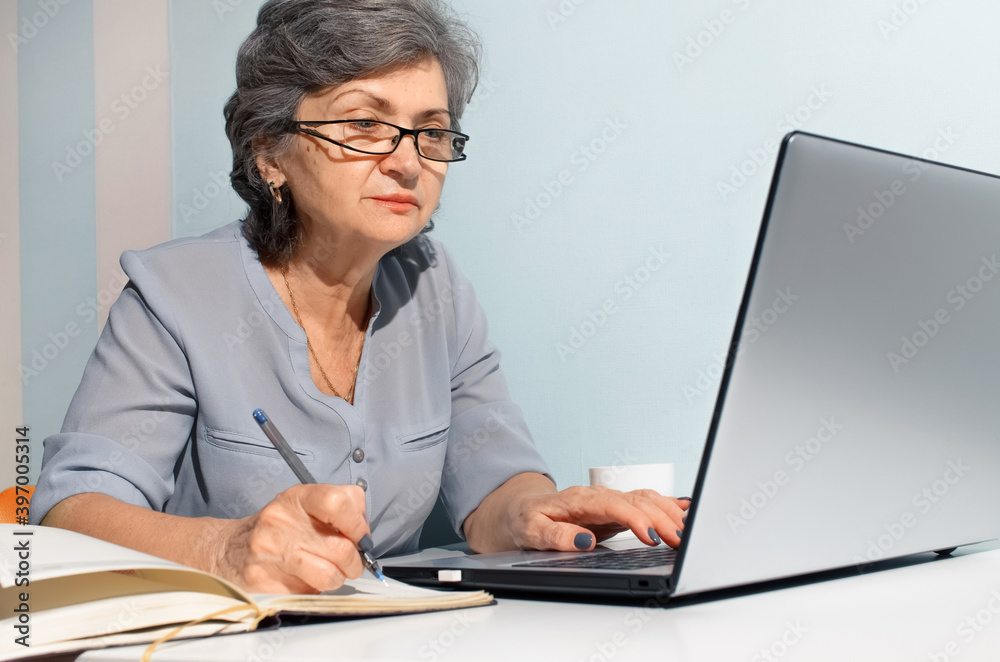 Elderly woman using laptop and writing in diary. Concept of telecommuting, freelancing, retired work Elderly woman using laptop and writing in diary. Concept of telecommuting, freelancing, retired work