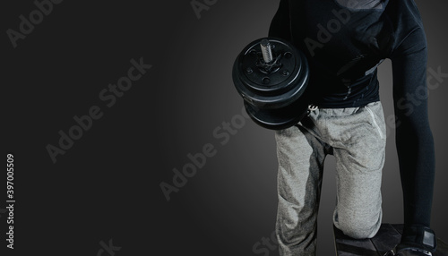 A man performs exercises using weights on a dark, black background. The concept of sports and taking care of your figure.