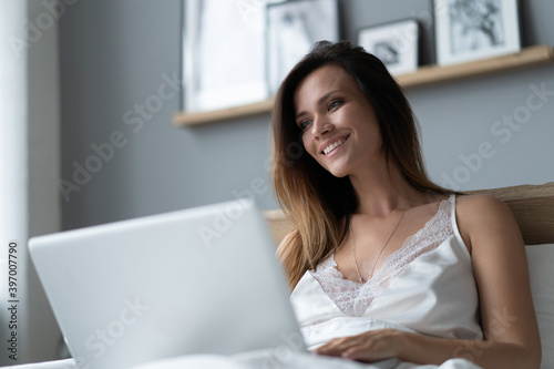 Pretty woman using her laptop in bed.