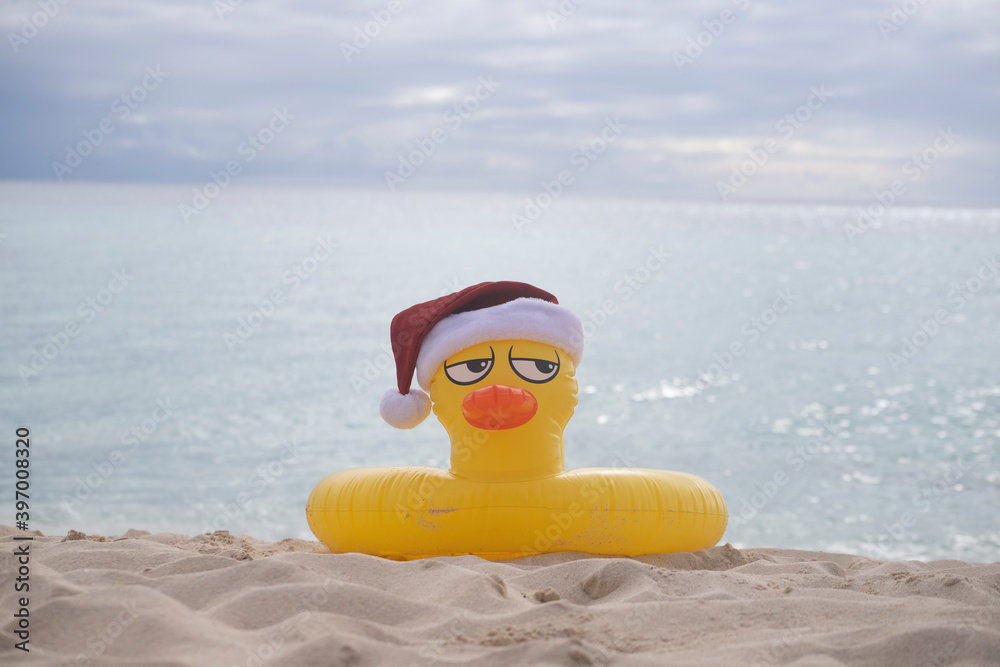 Naklejka premium YELLOW INFLATABLE LIFEGUARD DUCK WITH SANTA CLAUS HAT ON THE SHORES OF A CARIBBEAN BEACH ON A SUNNY DAY