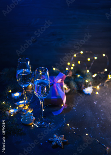 Romantic Christmas evening greeting card. Two glasses of champagne, gift box, bright glowing color holiday decor