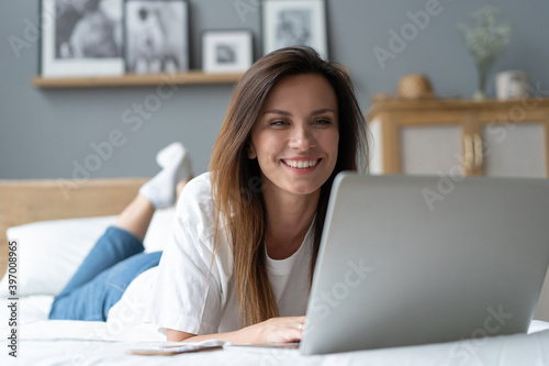 Portrait of a beautiful smiling young woman using laptop in bed at home.