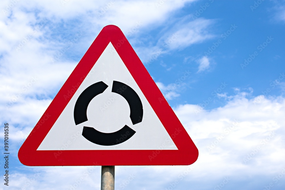 Road traffic the UK sign Roundabout ahead, against a blue cloudy sky. Road traffic the UK sign Roundabout ahead, against a blue cloudy sky.