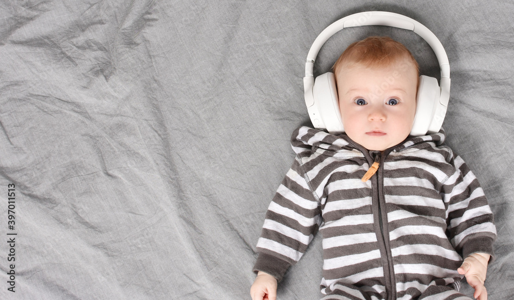 Amazed, three-four months old cute caucasian baby lying on bed listening to music in big headphones. Enjoy music concept. Copy space. Look at camera. Amazed, three-four months old cute caucasian baby lying on bed listening to music in big headphones. Enjoy music concept. Copy space. Look at camera.
