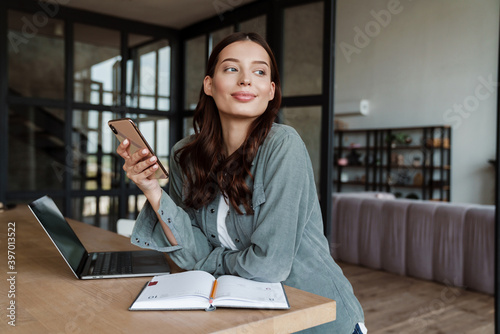 Obraz na plátně Beautiful smiling woman using cellphone while working with laptop