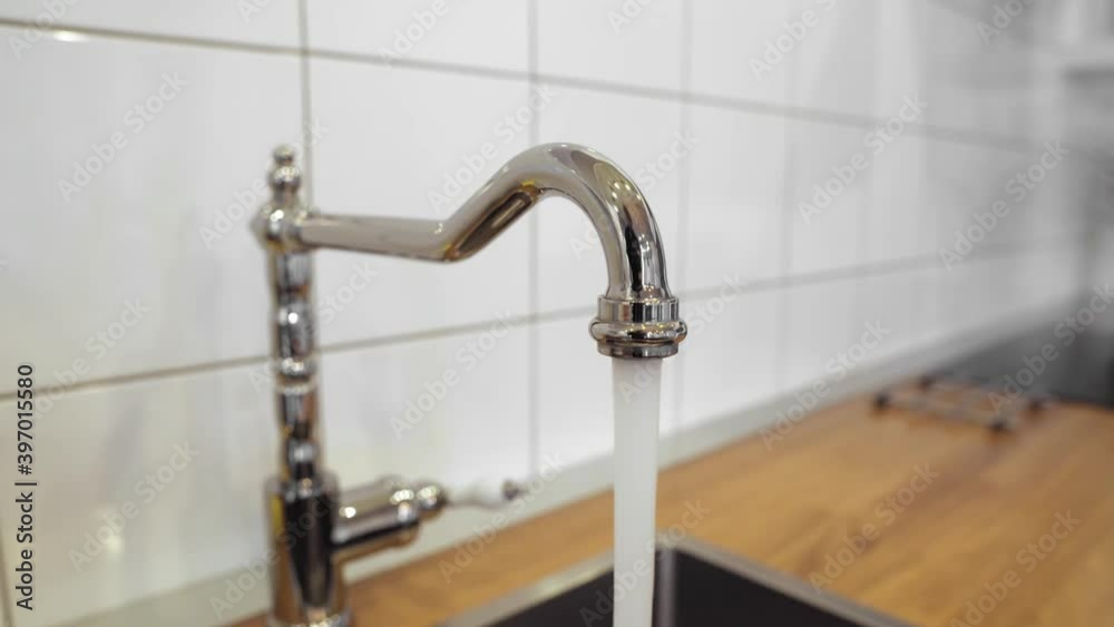 man filling a glass of water from a stainless steel kitchen tap