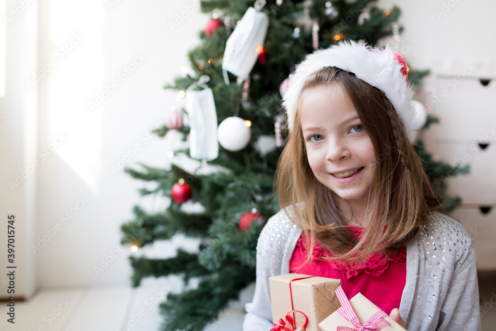 Young pretty girl in santa clause hat with Christmas gifts in front of a Christmas tree with masks Young pretty girl in santa clause hat with Christmas gifts in front of a Christmas tree with masks