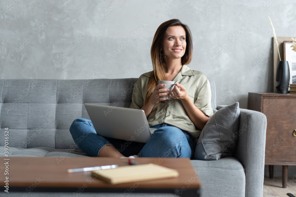 Naklejka premium Woman using a laptop in her living room. Working from home in quarantine lockdown. Social distancing.