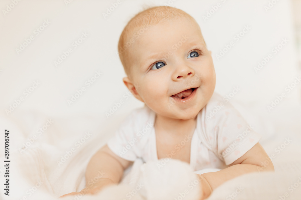 Portrait of wonderful baby girl laying on comfortable bed at home, adorable cute toddler look around with big interest, smiling, childhood and childcare concept