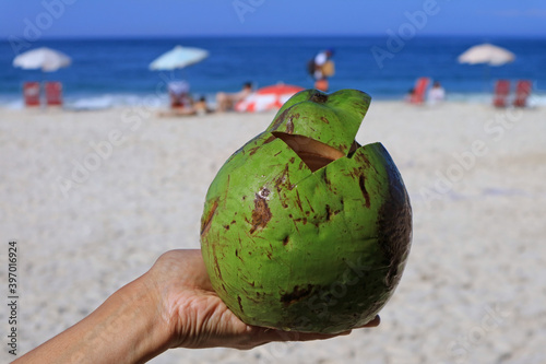Fresh young coconut on hand with blurry sandy beach and blue sea in background