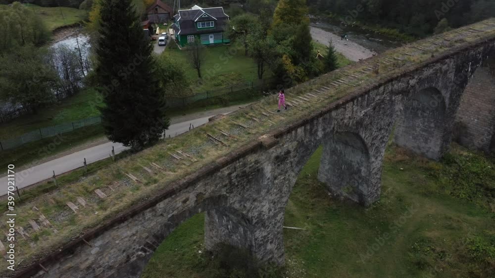 Aerial shot view of afro-american female athlete running along the old railway bridge in spectacular landscape. Active sports. Marathon preparation. Runner lifestyle. Aerial shot view of afro-american female athlete running along the old railway bridge in spectacular landscape. Active sports. Marathon preparation. Runner lifestyle.