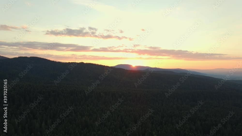 Lens flare in mountains at orange sunset in summer morning aerial view drone. Sun rays. Green pine forest slopes of mountain range. Bright disk of sun in blue sky slowly sets tops of mountains. Nature Lens flare in mountains at orange sunset in summer morning aerial view drone. Sun rays. Green pine forest slopes of mountain range. Bright disk of sun in blue sky slowly sets tops of mountains. Nature