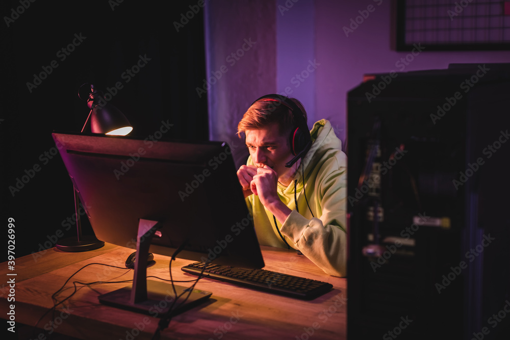Tensed gamer in headset looking at computer monitor during video game at home