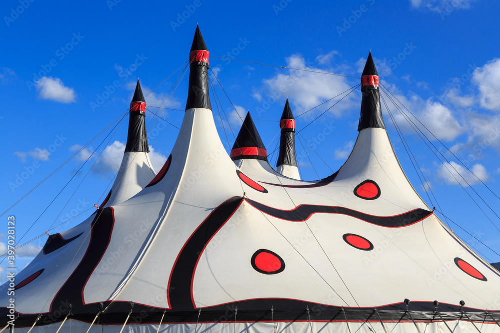 A white big top circus tent, with many spires and a pattern of red dots and black swirls

