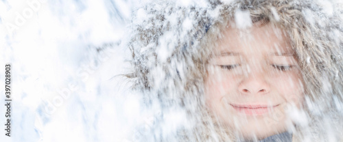 Child face with closed eyes smiling with blurred snow falling. Banner