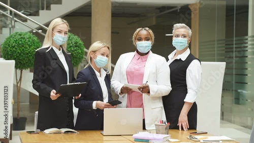 Group of colleagues in medical masks in office, they look at camera, during coronavirus pandemic.