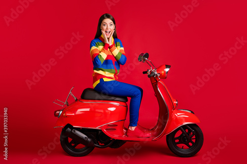Portrait of charming cheerful amazed girl sitting on moped having fun great sale isolated over bright red color background