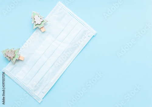 medical protective face mask and figures of Christmas trees and snowflakes wooden on a blue background. Decor Christmas and New Year 2021. Holidays self-isolation and coronavirus pandemic concept