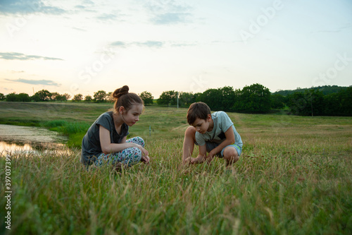Photo of a girl and a boy that founded something on the ground with a landscape in the back