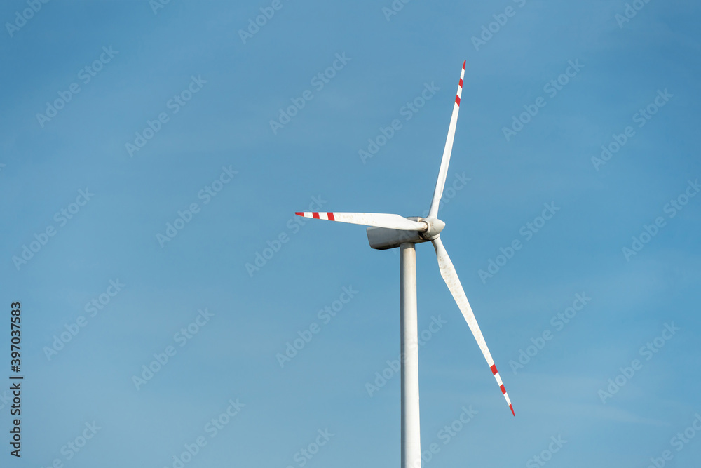 view of a modern windmill against a blue sky. The white blades of the wind turbine close up. Renewable energy source. Production of cheap and safe electricity.
