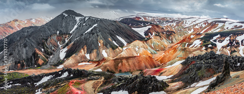 Panoramic amazing Icelandic landscape of colorful rainbow volcanic Landmannalaugar mountains, at famous Laugavegur hiking trail with dramatic snowy sky, and red volcano soil in Iceland