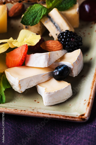 Cheese plate served with grapes and nuts. Assorted cheeses camembert, brie, parmesan blue cheese, goat with grapes, gressini sticks, cashews, honey and jam. photo