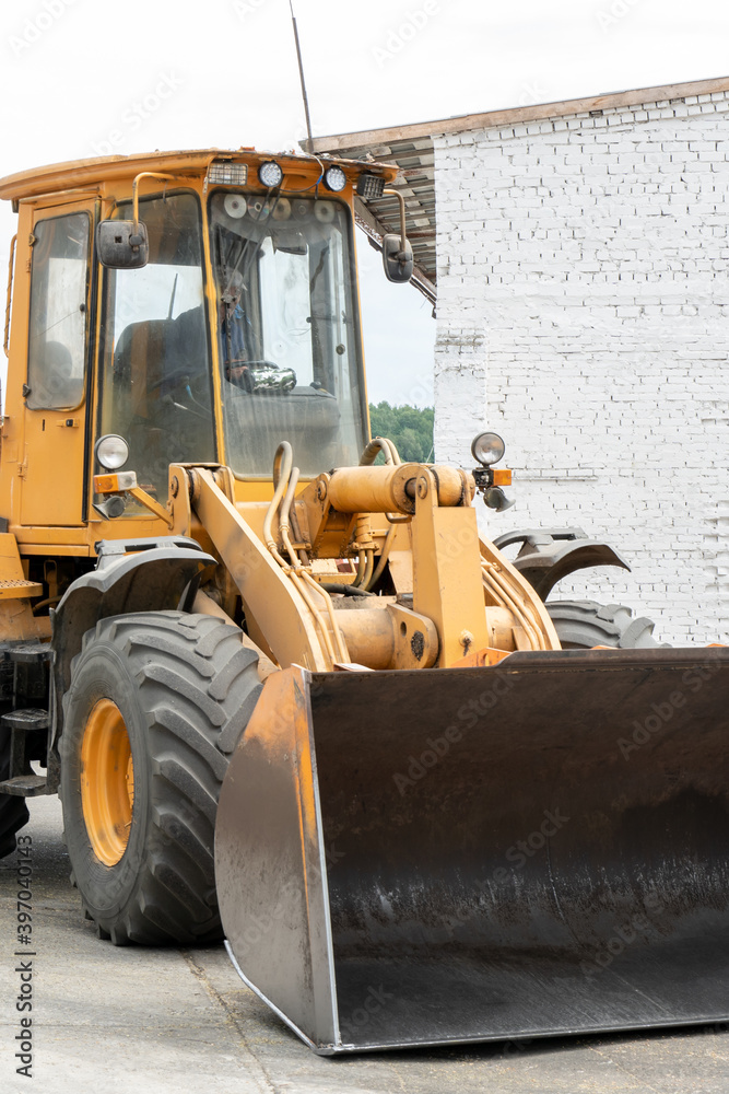 Obraz premium The excavator loads grain with a large bucket for processing and drying in the agro manufacturing plant of agricultural products. Iron barrels with grain and grain silos of the Elevator. Silver silos