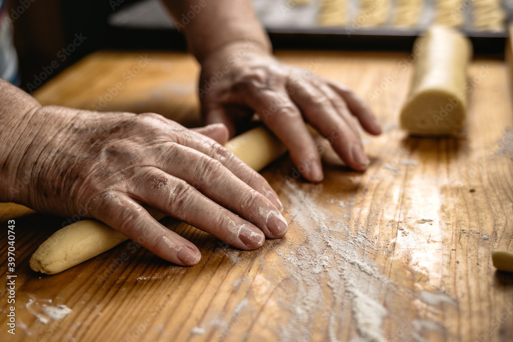 Senior woman is rolling pastry dough by hand. Preparing vanilla crescent rolls on wooden board. Cooking traditional christmas sweets