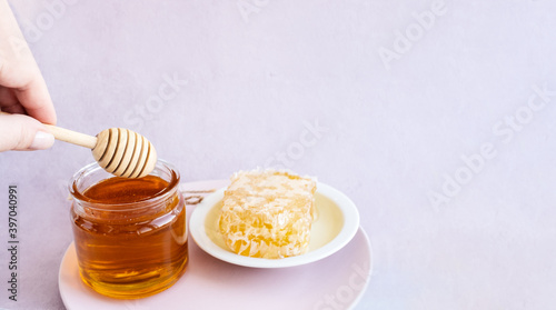 glass jar full of honey, plate with honeycomb on light brown background