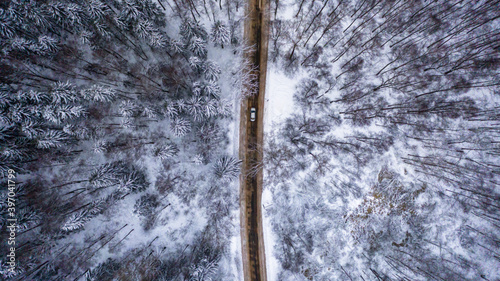 Aerial view of a car moving in the daytime, in winter, through a snow-covered forest road