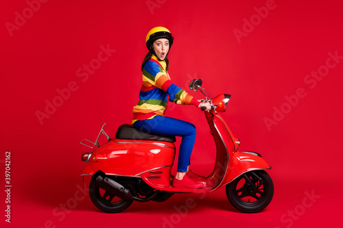 Photo portrait of shocked girl riding retro scooter isolated on vivid red colored background