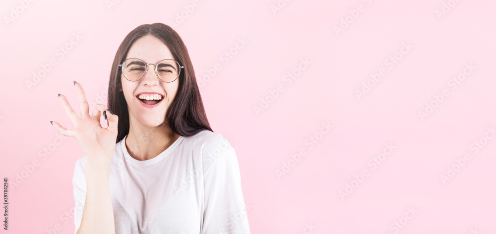 Girl with long black hair winking, smiling and showing OK sign over pink backgrund with copyspace. Girl with long black hair winking, smiling and showing OK sign over pink backgrund with copyspace.