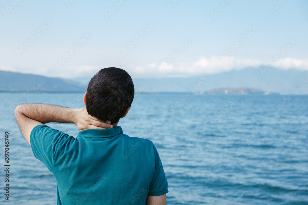 Male tourist touching neck and enjoying view of blue sea during summer travel Male tourist touching neck and enjoying view of blue sea during summer travel