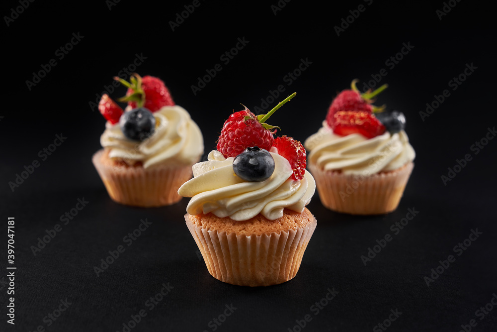 Tasty cupcakes with berries and cream, isolated on black.