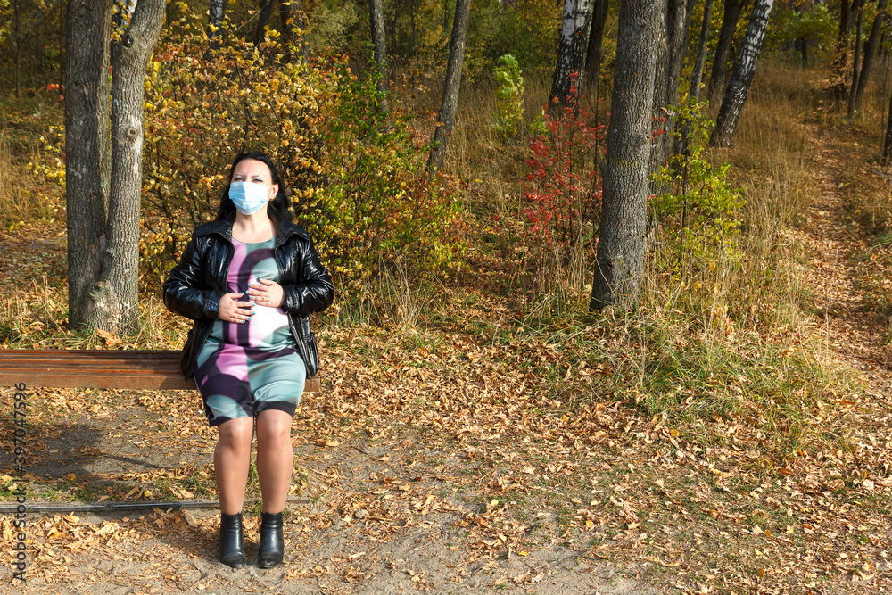 pregnant woman in autumn on a park bench in a protective mask stroking her belly with her hands. pregnant woman in autumn on a park bench in a protective mask stroking her belly with her hands.
