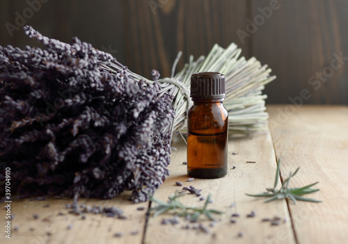 Lavender essential oil in the bottle with lavender bouquet and herb leaves nearby on rustic wooden table, closeup, copy space, natural cosmetics, aromatherapy and naturopathy concept