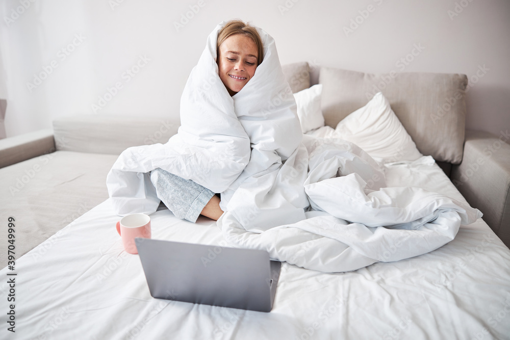 Cheerful young woman using laptop in bedroom