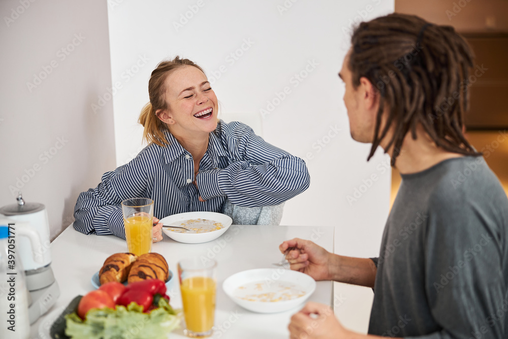 Happy young couple having breakfast in kitchen at home
