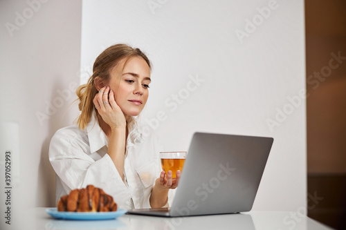 Beautiful young woman drinking tea and using laptop