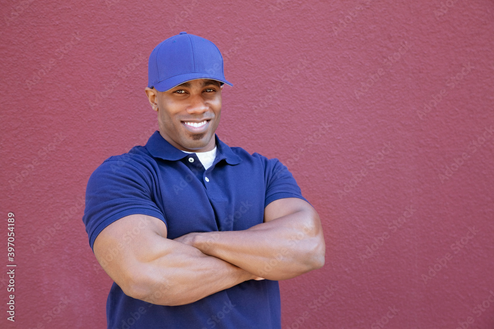 Portrait of a muscular African American delivery man with arms crossed over colored background Portrait of a muscular African American delivery man with arms crossed over colored background