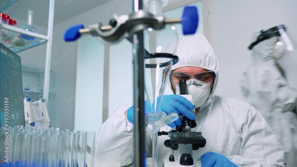 Medical research scientist conducting DNA experiments under microscope wearing protection suit in laboratory. Chemist examining virus evolution using high tech for vaccine development against covid19 Medical research scientist conducting DNA experiments under microscope wearing protection suit in laboratory. Chemist examining virus evolution using high tech for vaccine development against covid19