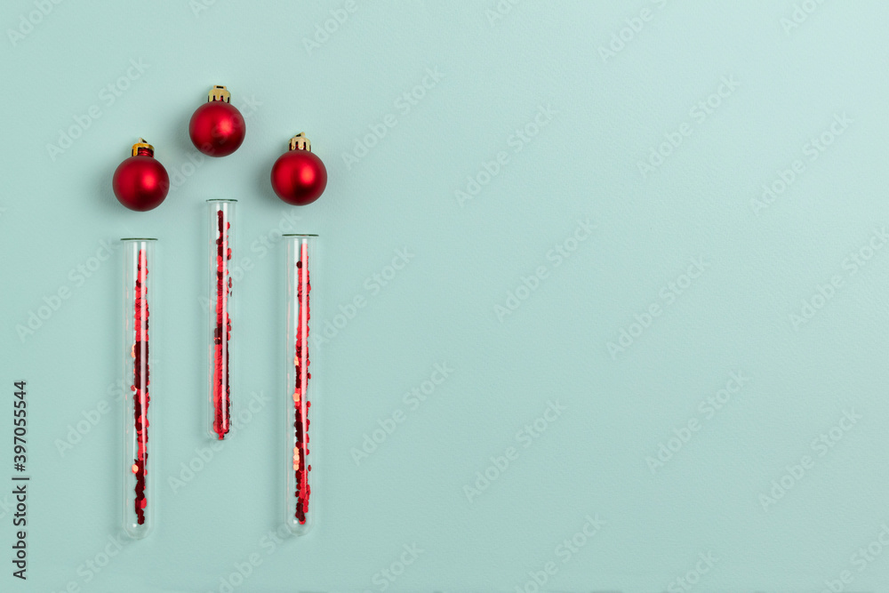 Medical test tubes with red sparkles inside lie next to Christmas balls on a mint green background. Festive flat lay with copy space. Medical test tubes with red sparkles inside lie next to Christmas balls on a mint green background. Festive flat lay with copy space.