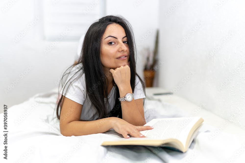 Young beautiful woman lying on bed while reading book Young beautiful woman lying on bed while reading book