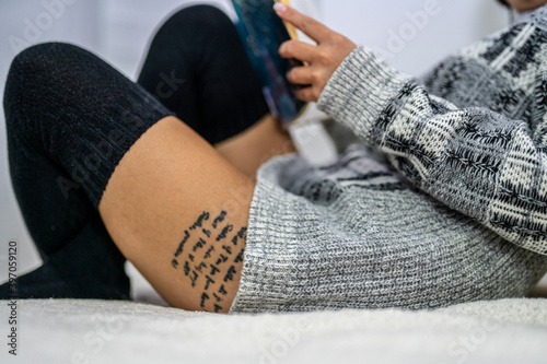 Close up of young tattooed woman in sweater and kneesocks on sofa while reading book