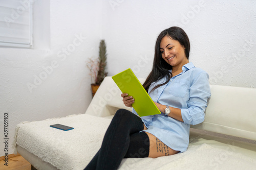 Beautiful woman wearing button down shirt and kneesocks while sitting on sofa and using tablet photo